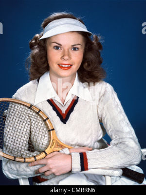 Negli anni quaranta anni cinquanta ritratto giovane donna indossa abbigliamento da tennis VISOR HOLDING racchetta in legno guardando la fotocamera Foto Stock