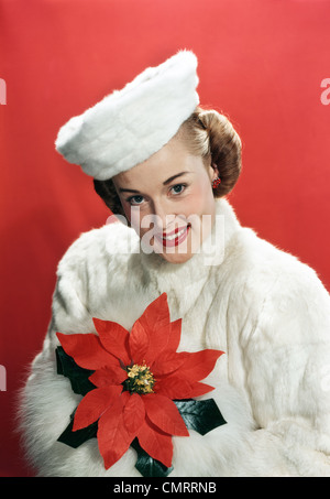 1940s ritratto sorridente donna che indossa la pelliccia bianca soprabito e HAT HOLDING POINSETTIA guardando la fotocamera Foto Stock