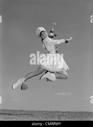 Anni sessanta donna MAJORETTE indossano uniformi di banda tenendo BATON saltare in aria Foto Stock