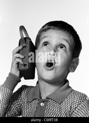 Anni sessanta BOY HOLDING radio a transistor fino al suo orecchio mentre canta insieme Foto Stock