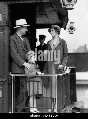 Negli anni Trenta una famiglia di tre persone in piedi alla ringhiera di protezione sul retro della carrozza del treno con facchini IN BACKGROUND Foto Stock