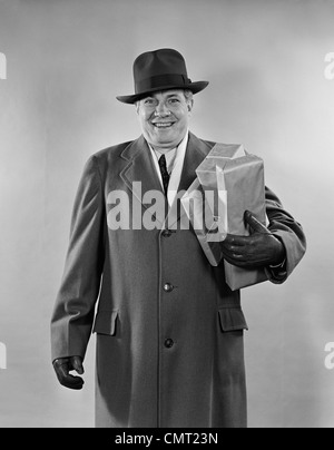 Negli anni quaranta anni cinquanta uomo sorridente CHE TRASPORTANO LE CASELLE DELLO SHOPPING INDOSSANDO HAT rivestire i guanti guardando la fotocamera Foto Stock