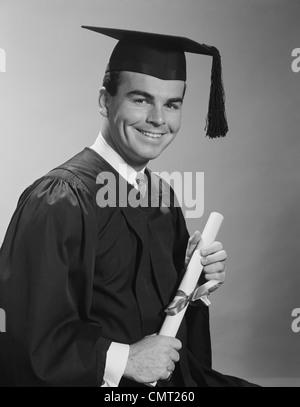 Anni sessanta uomo sorridente HOLDING DIPLOMA indossa vesti di graduazione Foto Stock
