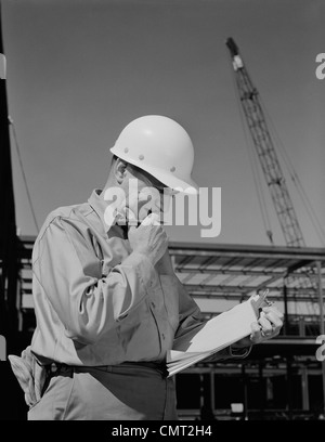 Negli anni sessanta la costruzione maschio Supervisore Cantiere INDOSSARE ELMETTO LA LETTURA DI DOCUMENTI Foto Stock