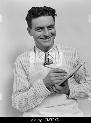 1930s 1940s sorridente CAPELLI RICCI uomo che indossa il grembiule facendo  ordine con matita e appunti guardando la fotocamera Foto stock - Alamy