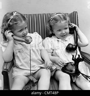 1930s 1940 TWIN BAMBINE sorelle insieme a parlare sul reale e telefoni giocattolo sorridente insieme seduti in poltrona Foto Stock