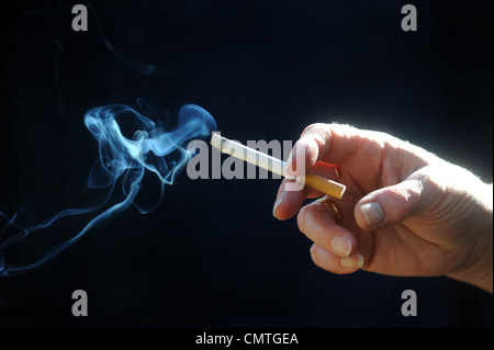 Sigaretta accesa tenuto in mano donna RE fumatori di fumare sigarette avvertenze sanitarie malattia cancro pericoli LIFETSTYLE SANO REGNO UNITO Foto Stock
