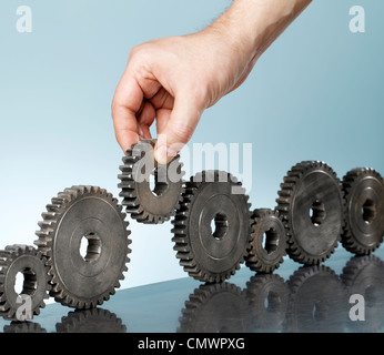 L'uomo aggiungendo un dente ingranaggio in una fila di vecchi ingranaggi cog. Foto Stock