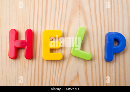 Lettera magnete HELP closeup su uno sfondo di legno Foto Stock