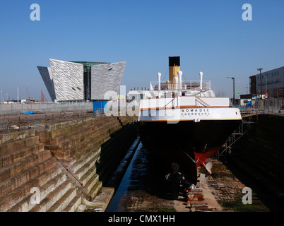 La nave nomadi si siede nel bacino di carenaggio con il Titanic Visitor Centre in background in Belfast, Irlanda del Nord Foto Stock