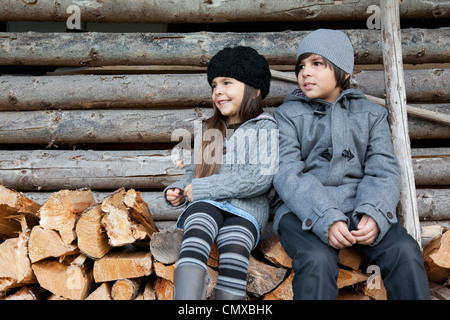 Germania, Huglfing, ragazza e ragazzo seduto sulla catasta di legna da ardere Foto Stock