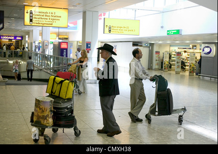 Passeggeri con bagaglio carrello all'area degli arrivi all'aeroporto di Heathrow Foto Stock