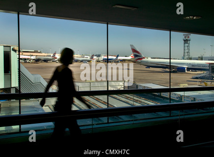 Donna oltrepassando la visualizzazione galleria all'aeroporto di Heathrow con British Airways aerei in background Foto Stock