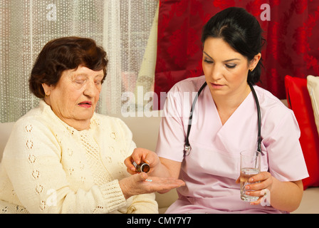 Medico dà pillole e acqua per senior paziente donna di casa sua Foto Stock