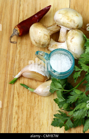 Aglio, Funghi, peperoncino, prezzemolo, cetriolo e spezie su un tagliere Foto Stock