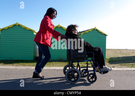 Regno Unito west sussex littlehampton una donna anziana ruote essendo in una sedia a rotelle passato capanne sulla spiaggia Foto Stock