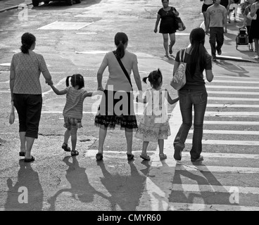 Adulti e bambini tenere le mani durante l'attraversamento di una strada nella Chinatown di New York City. Foto Stock