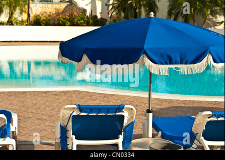 Ombrello blu e sedie allineate lungo una piscina. Foto Stock