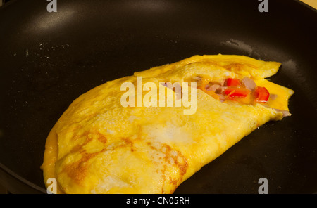 Una tre-frittata di uova per la cottura in una padella con ingredienti di riempimento visibile Foto Stock