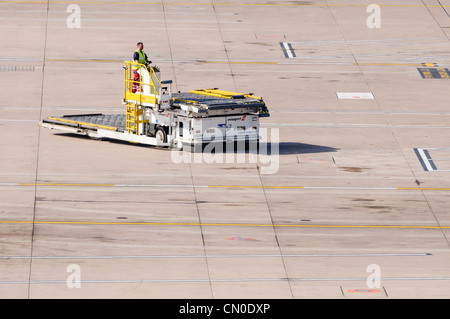 Aeroporto di trasportatore di contenitore essendo guidato su un aeroporto vuoto grembiule Foto Stock