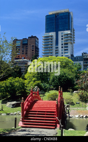 Tradizionale ponte rosso in legno su uno stagno nel Giardino Giapponese con alti edifici cittadini dietro Palermo, Buenos Aires, Argentina. Foto Stock