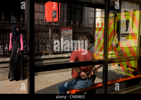 Le riflessioni di londinesi e riflette la parte posteriore di un NHS London ambulanza fermato vicino a un bus shelter. Foto Stock