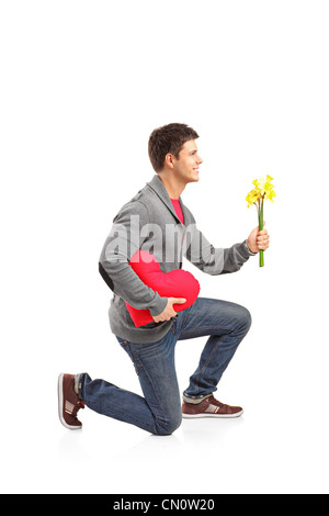 Un giovane uomo tenendo un cuore Cuscino sagomato e mazzo di fiori isolati su sfondo bianco Foto Stock