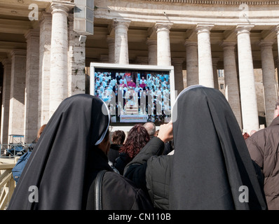 Due monache a guardare la TV con Papa Benedetto su un grande schermo TV al di fuori Basilica di San Pietro in Roma, Italia Foto Stock