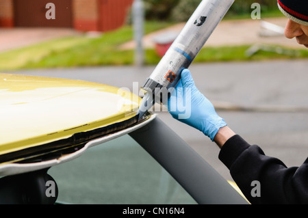 L uomo si applica la colla prima di montare un nuovo parabrezza di un auto Foto Stock