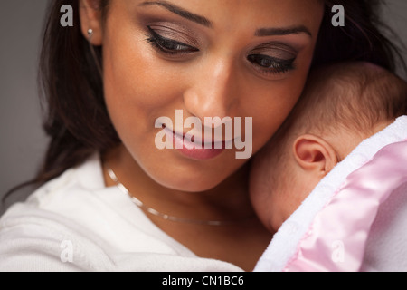 Giovane attraente donna etniche mentre tiene il suo neonato sotto illuminazione drammatica. Foto Stock