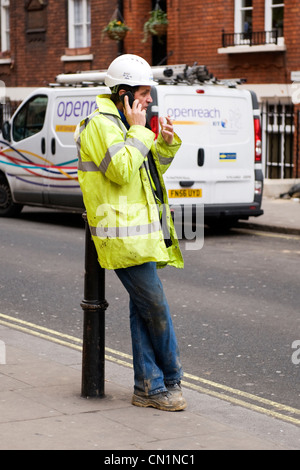 Oxford Street London West End British lavoratore operaio in hard hat day glow giacca a chattare su telefono cellulare appoggiata dal post Foto Stock