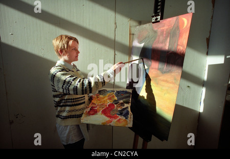 Una università di Brighton studente di belle arti dipinge un ritratto in studio come flussi di sole attraverso la finestra Creazione di ombre sulla parete Foto Stock