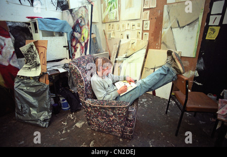 Maschio giovane studente di belle arti con i piedi fino in una caotica pittore's studio Foto Stock