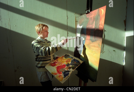 Una università di Brighton studente di belle arti dipinge un ritratto in studio come flussi di sole attraverso la finestra Creazione di ombre sulla parete Foto Stock