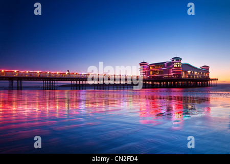 Twilight oltre il Grand illuminato dal molo Weston-Super-Mare, Somerset, Inghilterra, Regno Unito riflessa nella sabbia bagnata a marea alta. Foto Stock