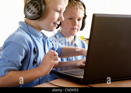 Due ragazzi della scuola di indossare le cuffie, guardando lo schermo del computer Foto Stock