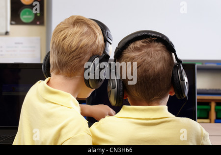 Due ragazzi della scuola di indossare le cuffie, guardando lo schermo del computer Foto Stock