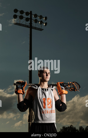 Giovane atleta holding lacrosse stick sotto i proiettori Foto Stock