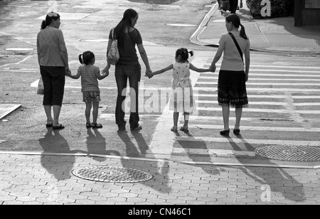 Adulti e bambini tenere le mani prima di attraversare una strada a Chinatown in New York City. Foto Stock