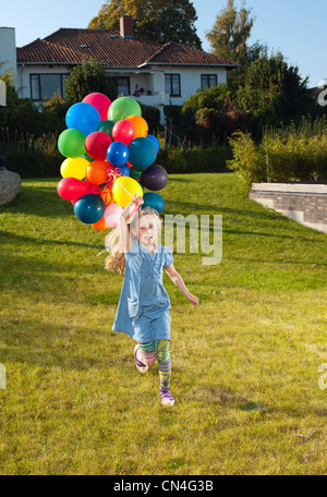 Ragazza che corre attraverso il prato con palloncini multicolori Foto Stock