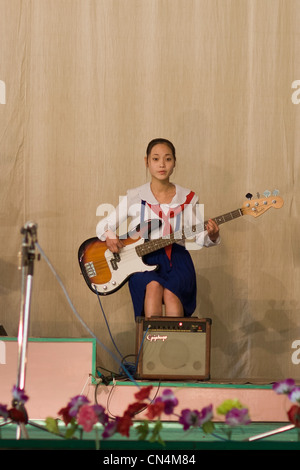 Corea del Nord Pyongyang, ragazza giovane a suonare la chitarra in una performance di giovani pionieri in un modello di scuola Foto Stock