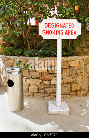 Prendere verticale di un libero segno permanente e portacenere di un pubblico zona fumatori nell'ombra di un angolo del giardino Foto Stock