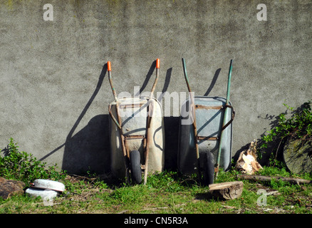 Due carriole appoggiata contro un muro esterno in un giardino Foto Stock