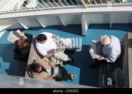 I passeggeri sulla Malta - Gozo ferry rilassarsi sul ponte leggendo quotidiani Foto Stock