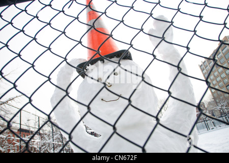 Un felice pupazzo di neve dietro una catena collegamento recinto. Foto Stock