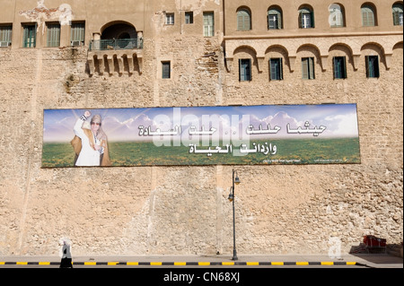 Libyan donna vestita di nero passeggiate passato a Tripoli billboard con la Libia è morto figura iconica, il Colonnello Muammar Gheddafi. Foto Stock