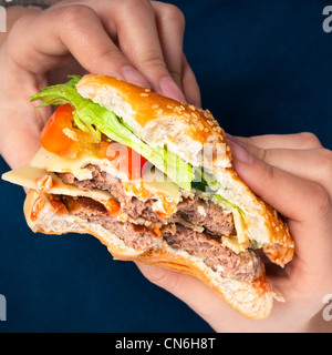 Close up di mani holding hamburger, su sfondo blu scuro. Foto Stock