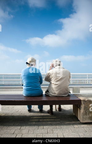 Vista posteriore di due anziani pensionati donna seduta su una panchina a Aberystwyth promenade, caldo pomeriggio a molla, Wales UK Foto Stock