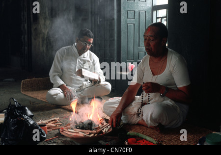 Un uomo è adorare un dio indù mentre un altro sta leggendo un libro sacro contenenti preghiere ( Nepal) Foto Stock