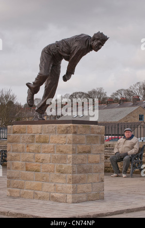 Uomo seduto su un banco di lavoro, guardando alla statua di bronzo di cricketer Fred (Freddie) Trueman (fast bower in azione posa) - Skipton, North Yorkshire, Inghilterra, Regno Unito. Foto Stock